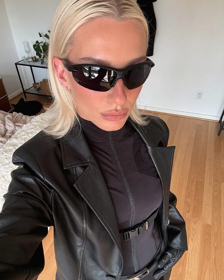 The same blonde woman in sunglasses, taking a selfie at home.